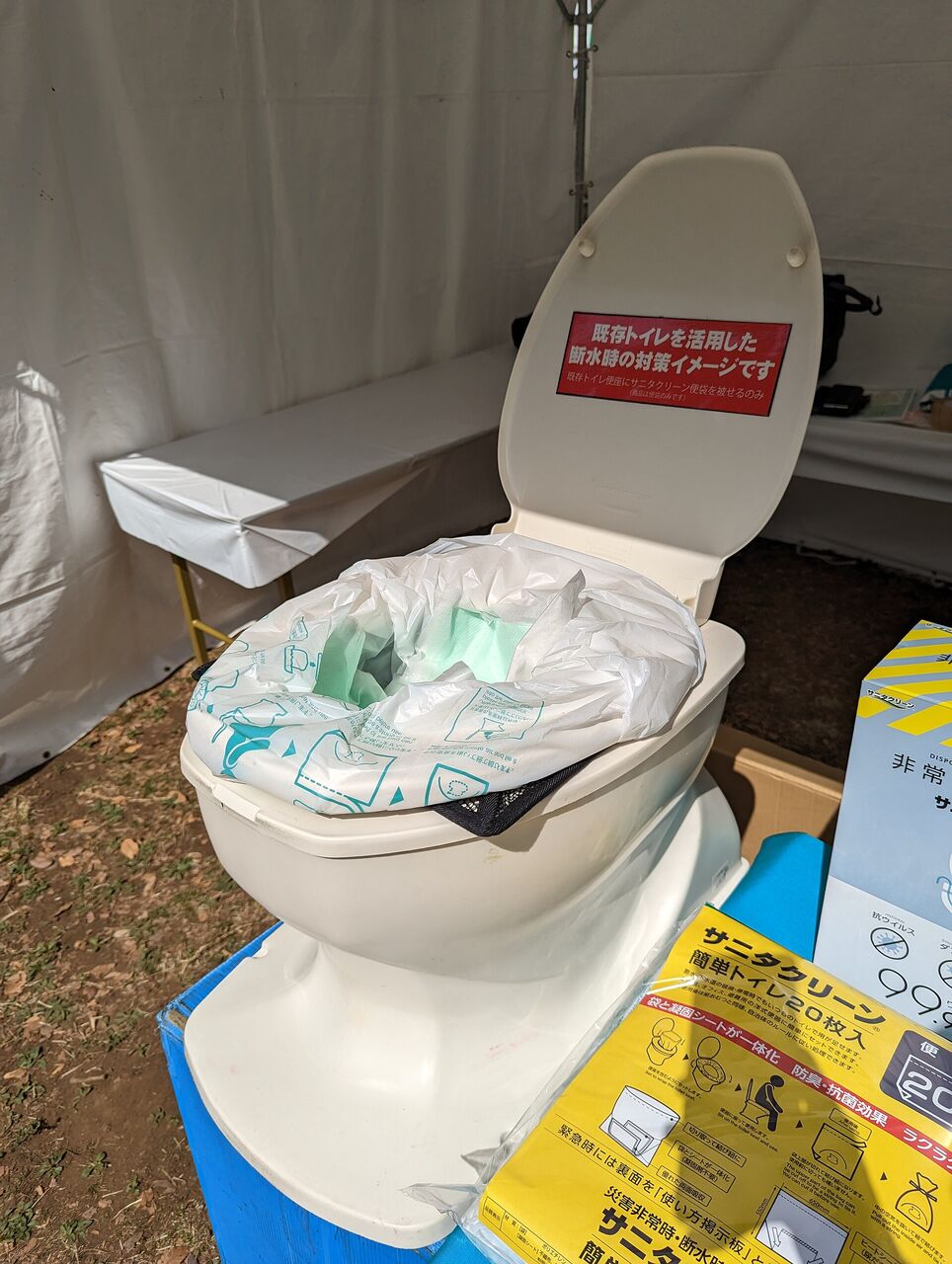 洋式の便器に、ポリ袋タイプの簡易トイレの袋がかぶせてある。手前に、簡易トイレの箱が見える