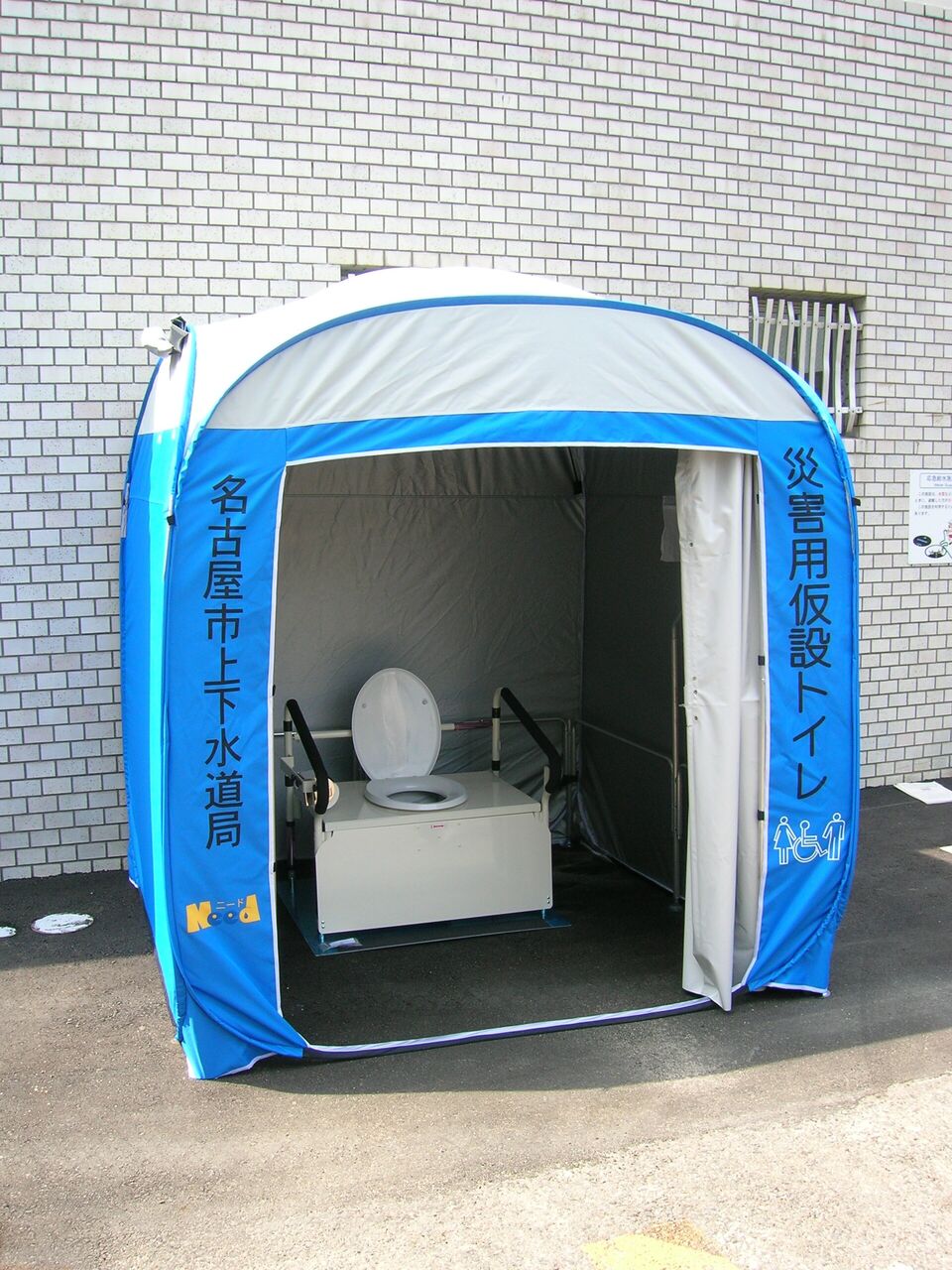 青と白のテントの中に、洋式の便器が置かれている。テントの側面に「災害用仮設トイレ」と書かれている