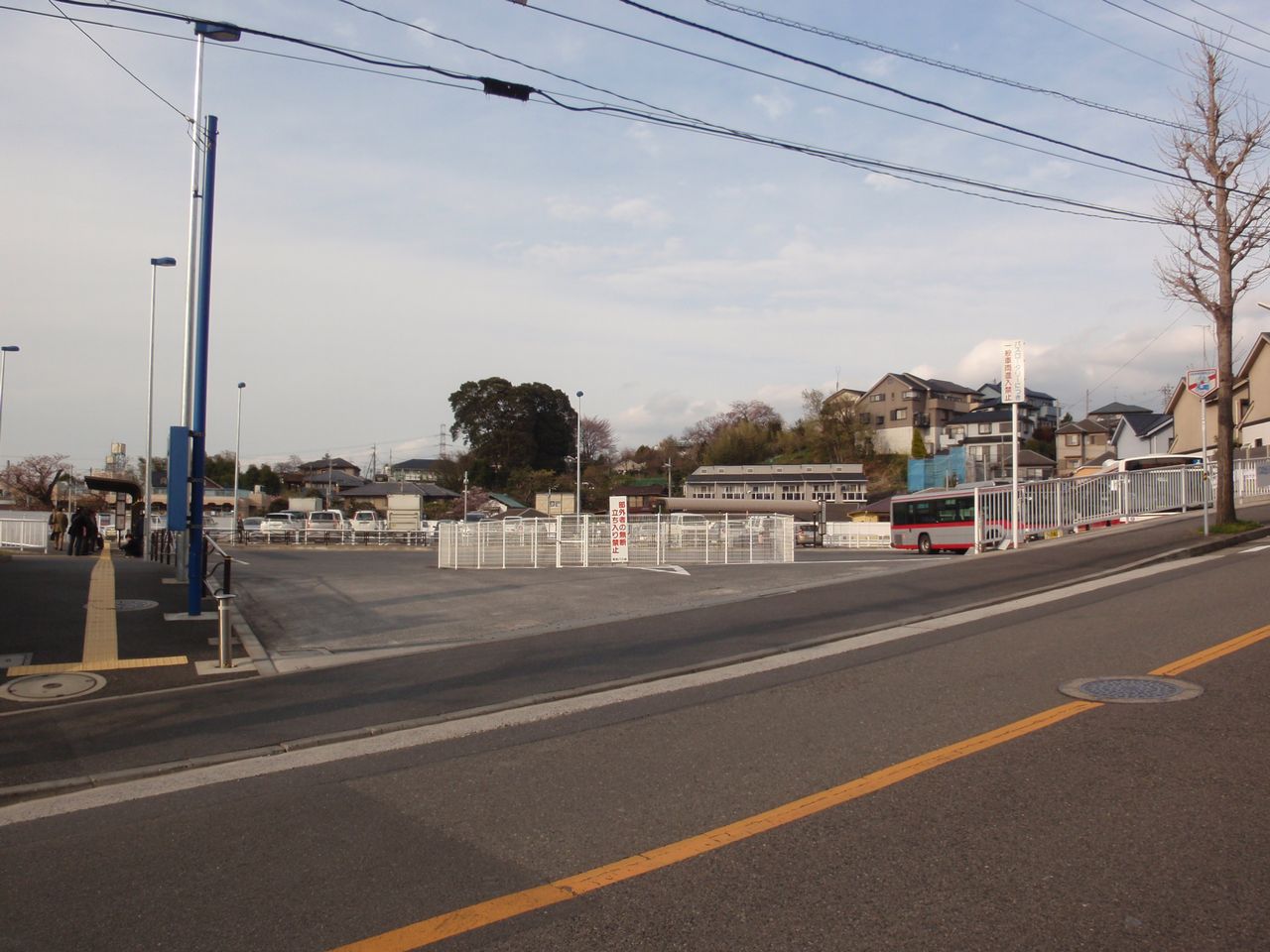 柿生駅南口のバスターミナル。広い舗装の広場に、赤い帯の市バスが1台とまっている