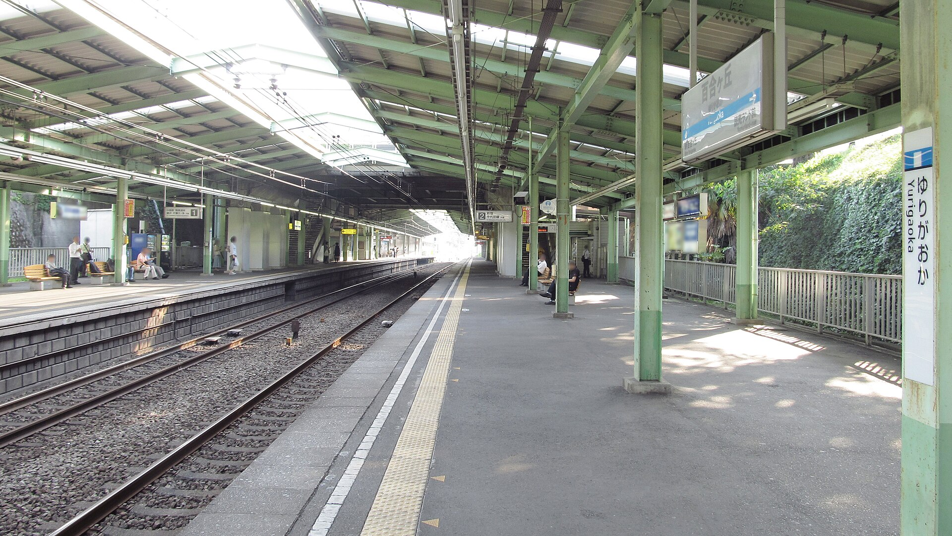 百合ヶ丘駅のホーム。緑色の柱と屋根が続き、柱に「ゆりがおか」の駅名標がある。右側は植物でおおわれた斜面