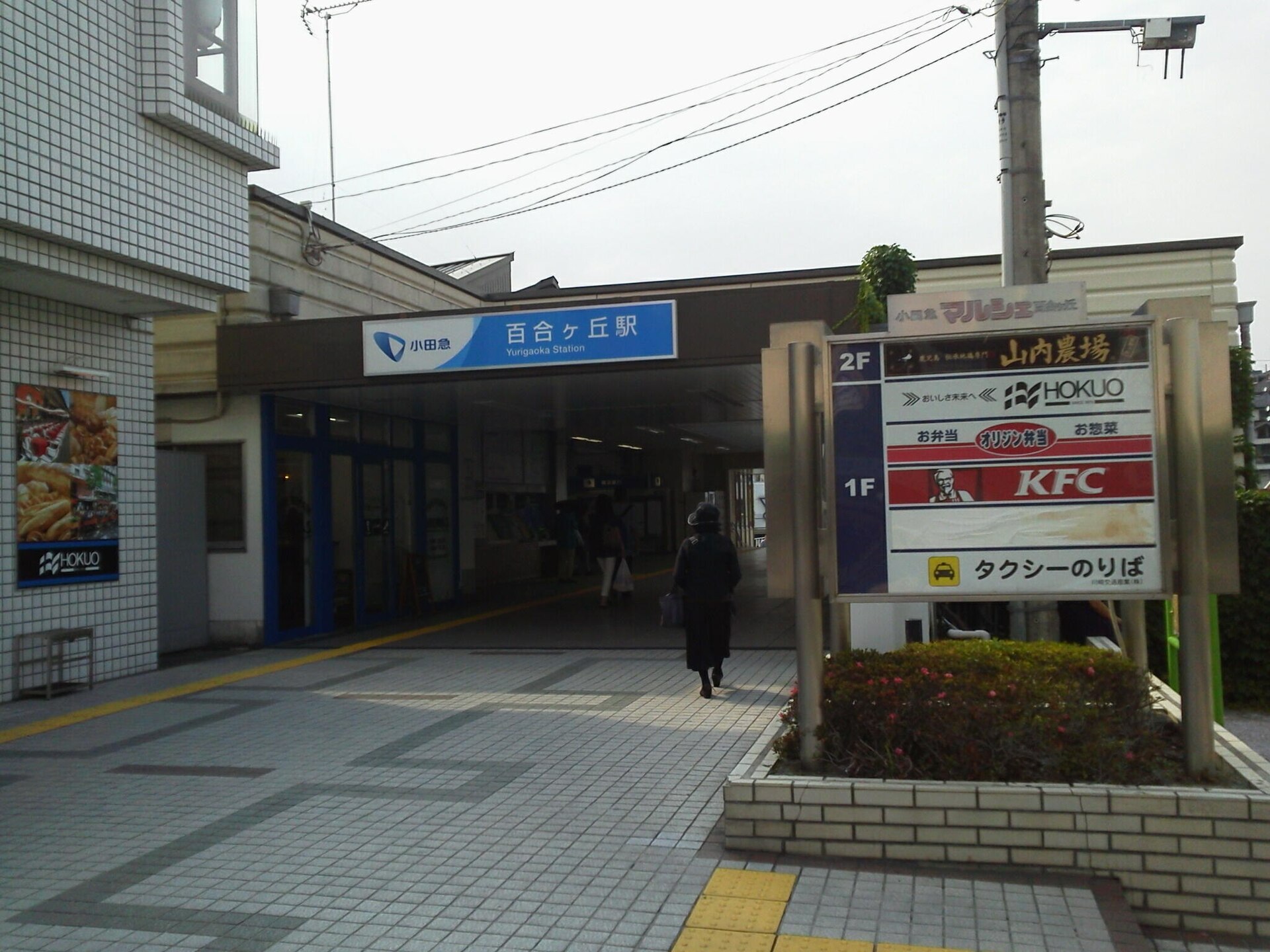 百合ヶ丘駅の南口。青い駅名の看板の下に改札へ続く通路があり、右に店の案内板とタクシーのりばの表示がある